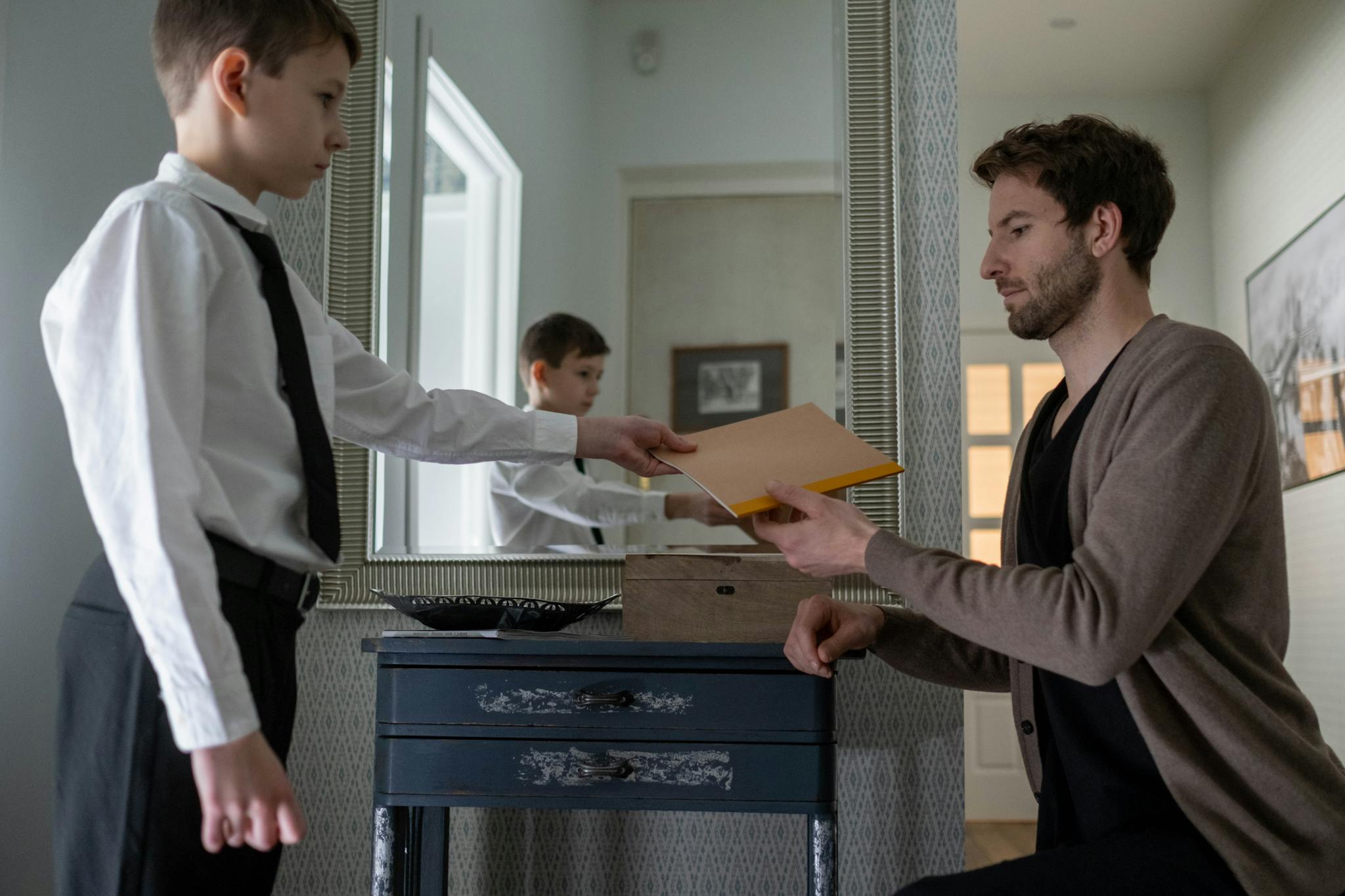 A father and son exchanging an envelope in an indoor setting, reflecting parenthood and communication.