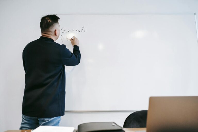 Instructor writing on a whiteboard in a classroom setting, showcasing educational engagement.